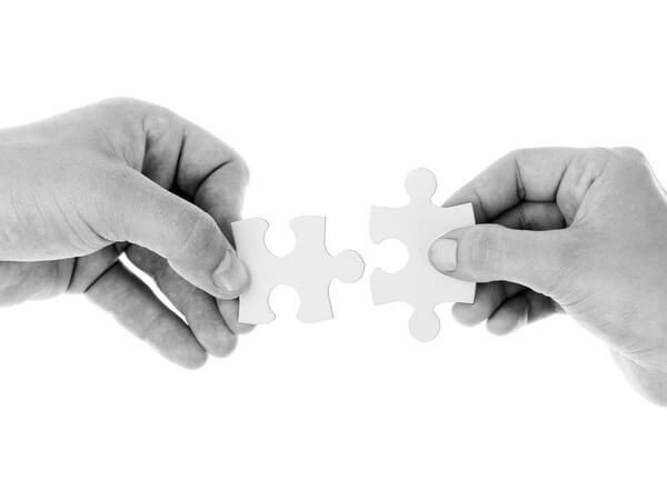 Manos montando piezas de puzle en blanco y negro.